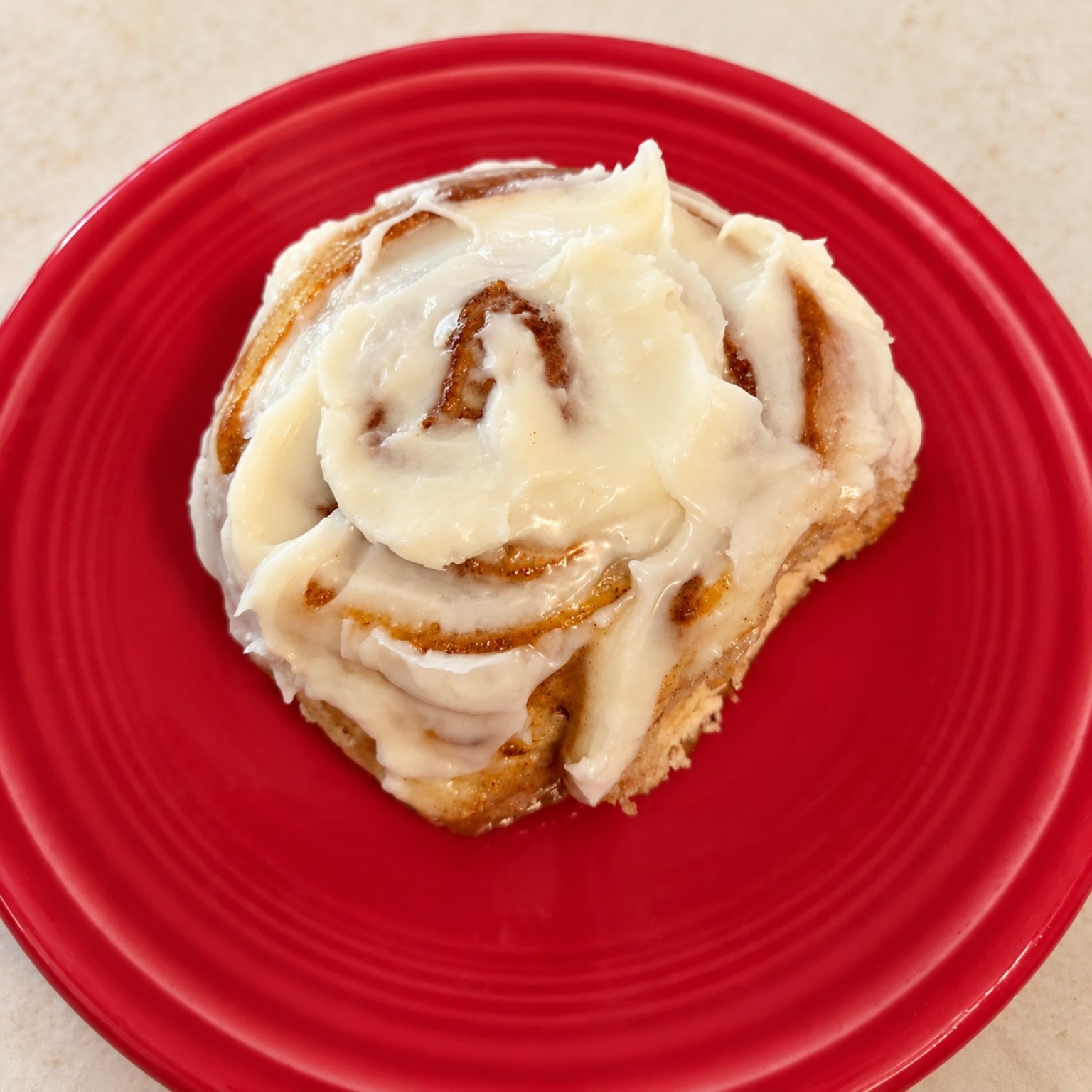 A homemade cinnamon roll generously covered in frosting on a red plate